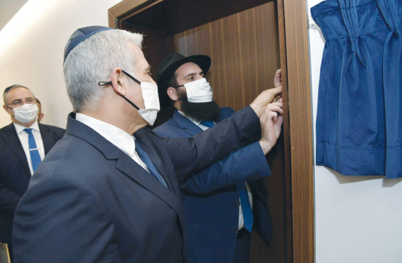 FOREIGN MINISTER Yair Lapid helps to affix a mezuzah to a doorpost of the Israeli Embassy in Abu Dhabi, UAE, last month. (credit: SHLOMI AMSALEM/GPO/REUTERS)