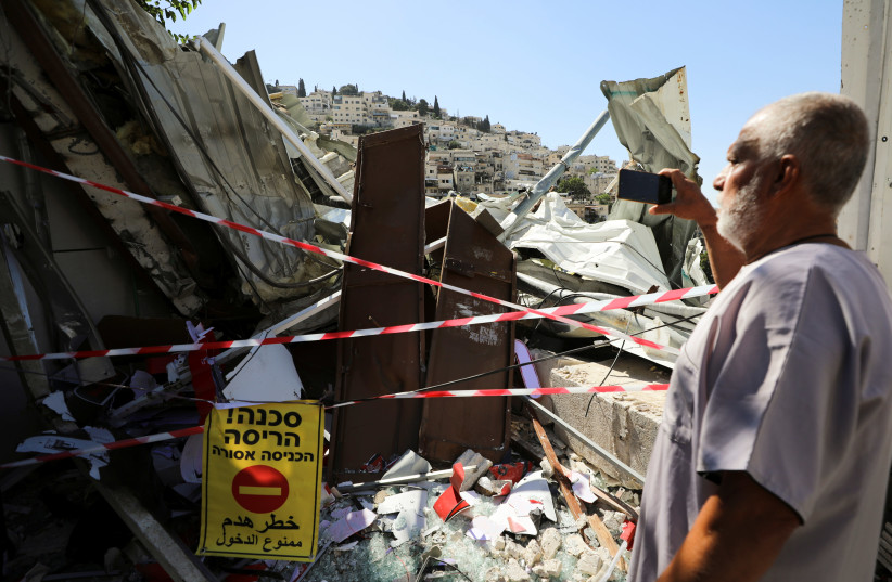 A Palestinian man uses his mobile phone as he stands near the debris of a shop that Israel demolished in the Palestinian neighbourhood of Silwan in East Jerusalem June 29, 2021 (credit: AMMAR AWAD / REUTERS)