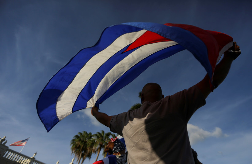 A man waves a Cuban flag as emigres gather outside Versailles restaurant, in reaction to reports of protests in Cuba against its deteriorating economy, in Miami, Florida, US July 18, 2021.  (credit: REUTERS/MARCO BELLO)