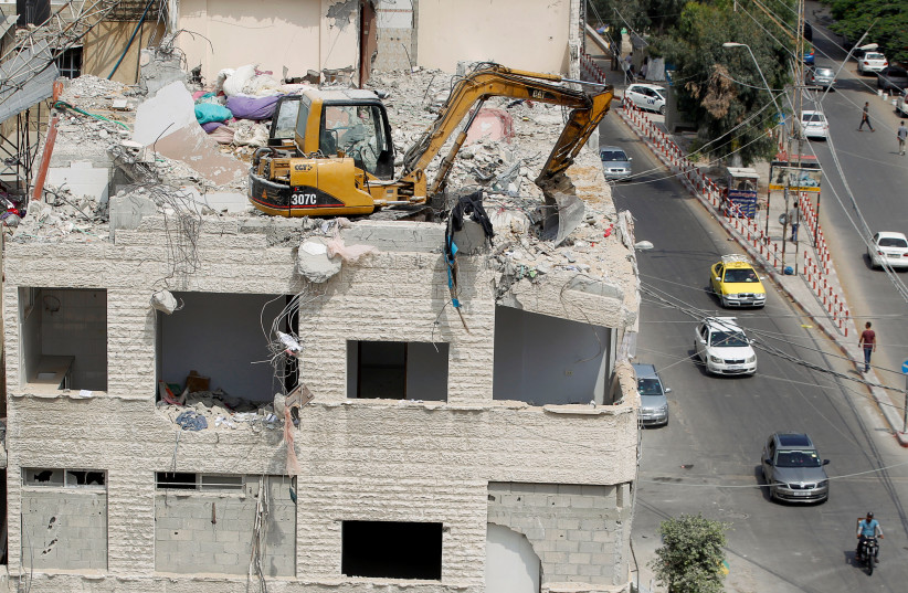 A machinery works to remove the debris atop a building damaged in Israeli air strikes during the fighting between Israel and Hamas, in Gaza City, July 25, 2021. (photo credit: MOHAMMED SALEM/ REUTERS)