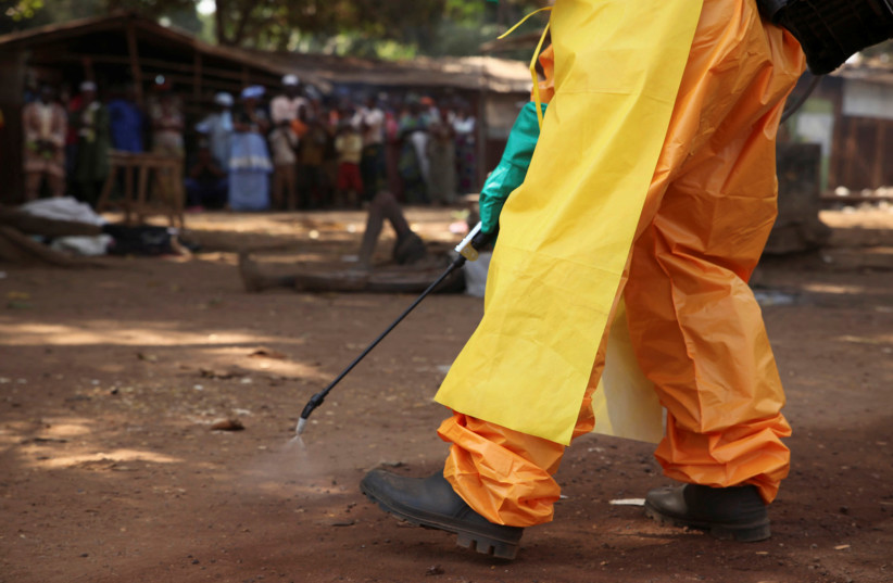  A member of the French Red Cross disinfects the area around a motionless person suspected of carrying the Ebola virus as a crowd gathers in Forecariah, Guinea. (photo credit: REUTERS)