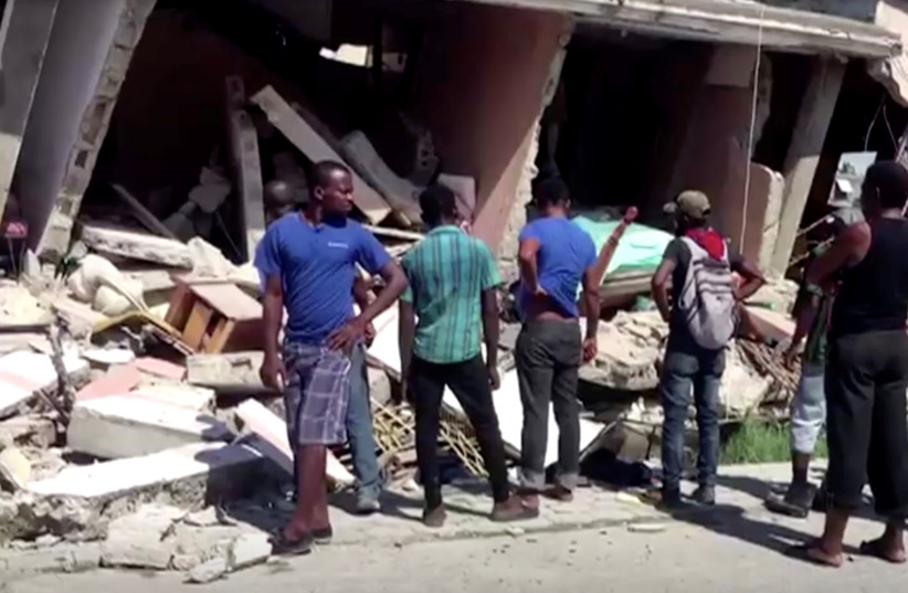  People stand in front of a collapsed building following an earthquake, in Les Cayes, Haiti, August 14, 2021 (credit: REUTERS TV)