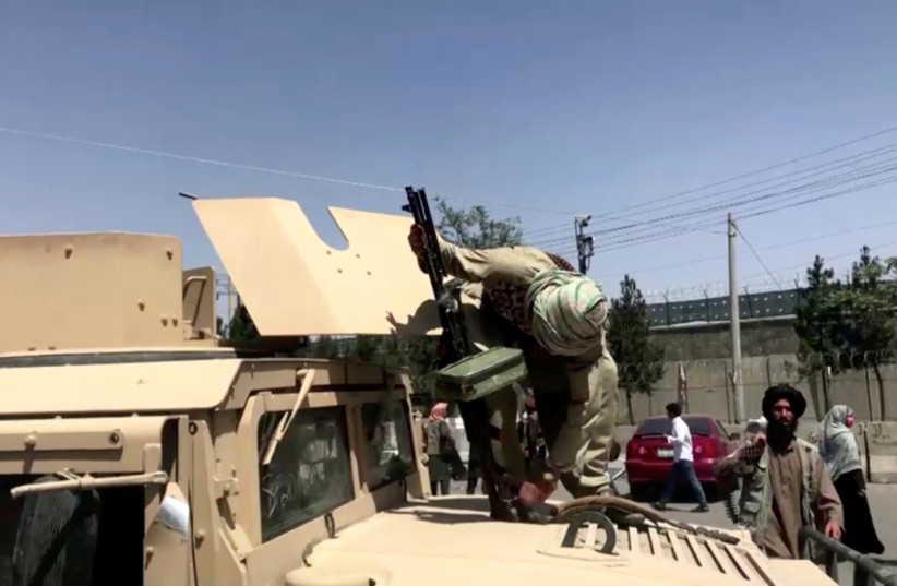 A Taliban fighter on top of an armoured vehicle loads a gun outside the airport in Kabul, Afghanistan August 16, 2021, in this still image taken from a video. (photo credit: REUTERS TV/via REUTERS)