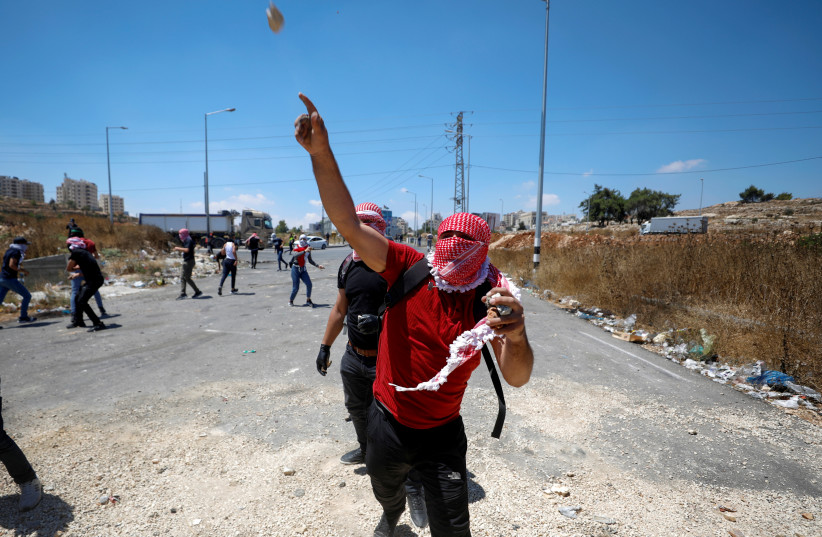  A Palestinian demonstrator hurls a stone at Israeli forces during a protest over the killing of four Palestinians by Israeli forces in a clash, near Israeli settlement of Beit El in the Israeli-occupied West Bank August 17, 2021 (photo credit: MOHAMAD TOROKMAN/REUTERS)