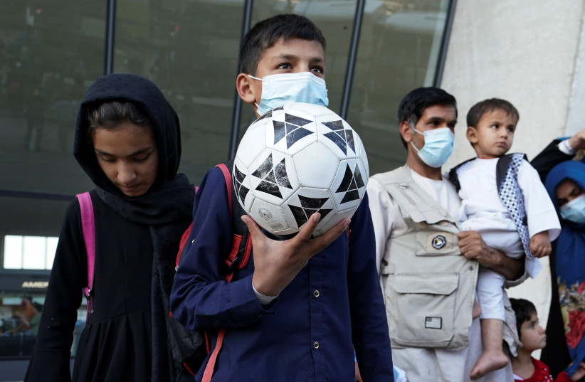  A boy holds a soccer ball as he and other Afghan refugees board a bus taking them to a processing center upon arrival at Dulles International Airport in Dulles, Virginia, US. (credit: KEVIN LAMARQUE/REUTERS)