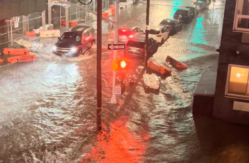  A vehicle moves along a flooded road as safety barriers float in floodwaters in Williamsburg, in the Brooklyn borough of New York City, New York, U.S. September 1, 2021, in this still image taken from video obtained from social media. (credit: JAYMEE SIRE/via REUTERS)