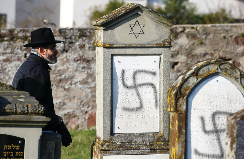  A MAN WALKS past graves desecrated with swastikas at the Jewish cemetery in Westhoffen, near Strasbourg, France, in 2019. (photo credit: REUTERS/ARND WIEGMANN)