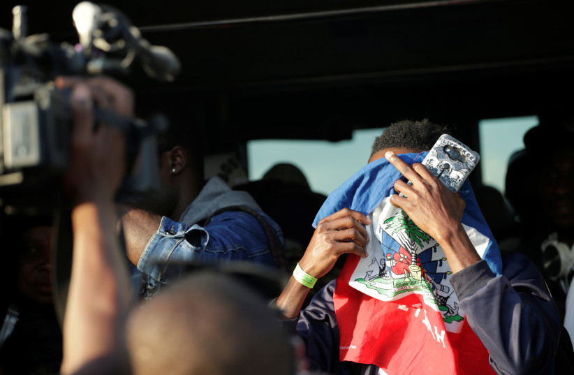  A Haitian man covers his face with a flag in front of cameras after descending from a Chilean Air Force plane upon his arrival to the International Airport of Port-au-Prince, Haiti, November 7, 2018. (credit: REUTERS/ANDRES MARTINEZ CASARES)