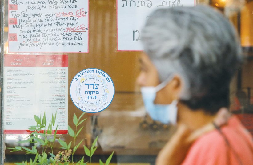  A WOMAN walks past a Jerusalem eatery with a Tzohar kashrut certificate. (credit: MARC ISRAEL SELLEM/THE JERUSALEM POST)