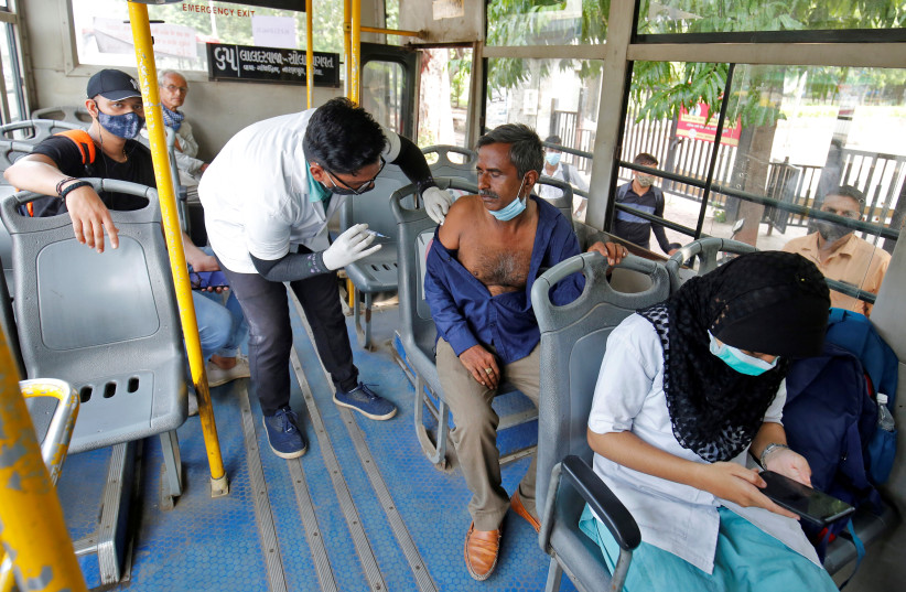  A man receives a dose of the COVISHIELD vaccine against the coronavirus disease (COVID-19), manufactured by Serum Institute of India, inside a passenger bus in Ahmedabad, India, September 23, 2021 (photo credit: REUTERS/AMIT DAVE)