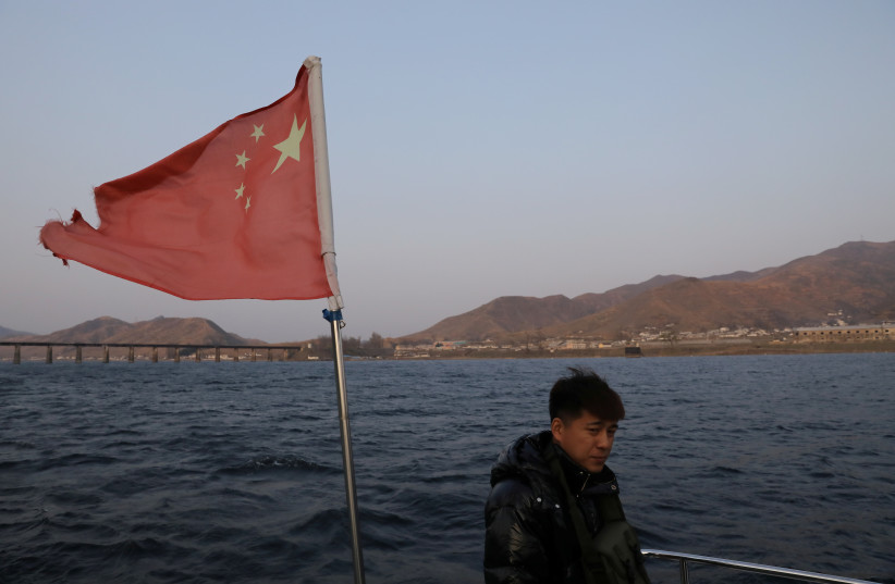  A man stands near a fluttering Chinese national flag on a cruise boat on the Yalu River separating North Korea and China, in Dandong, Liaoning province, China April 20, 2021. (photo credit: REUTERS/TINGSHU WANG)