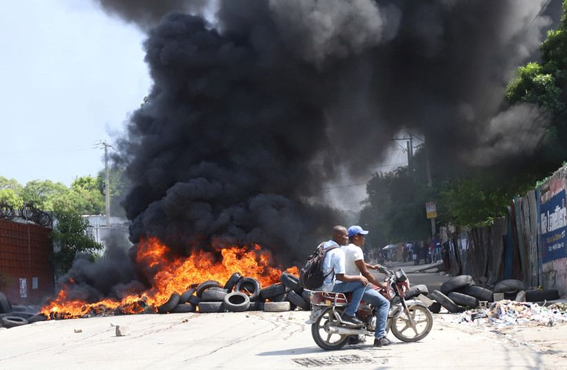  People ride on a motorcycle near a burning barricade as Haitians mount a nationwide strike to protest a growing wave of kidnappings, days after the abduction of a group of missionaries, in Port-au-Prince, Haiti October 18, 2021. (photo credit: REUTERS/RALPH TEDY EROL)