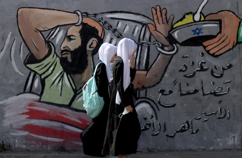  Palestinian students walk past a mural depicting hunger-striking Palestinian prisoner Maher Al-Akhras, Gaza Strip, October 19, 2020.  (photo credit: REUTERS/MOHAMMED SALEM/FILE PHOTO)