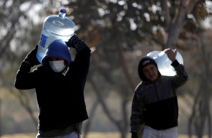  Migrants who traveled to northern Mexico seeking asylum in the United States, carry jugs of purified water at a migrant encampment in Matamoros, Mexico February 20, 2021. Picture taken February 20, 2021. (credit: REUTERS/DANIEL BECERRIL)