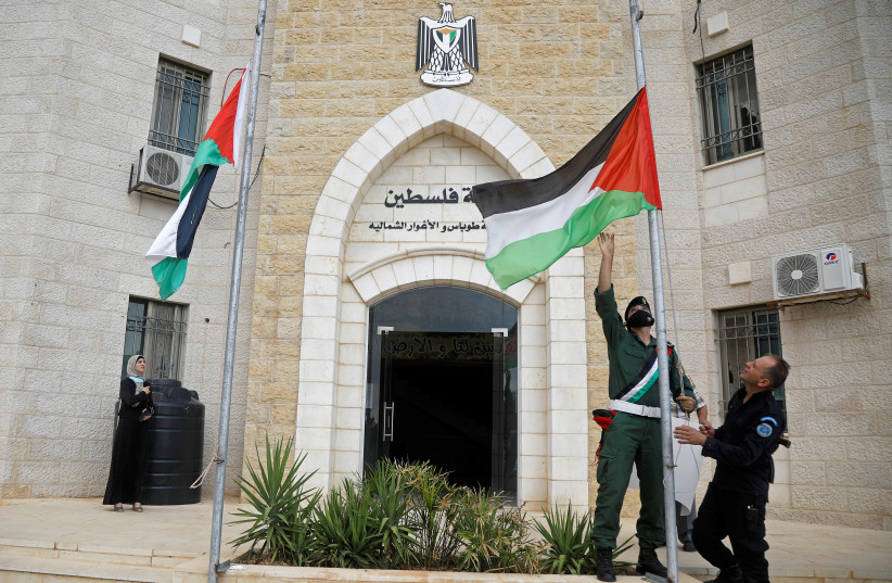 A member of security forces lower a Palestinian flag to fly at half-mast on November 10, 2020 (credit: REUTERS/RANEEN SAWAFTA)