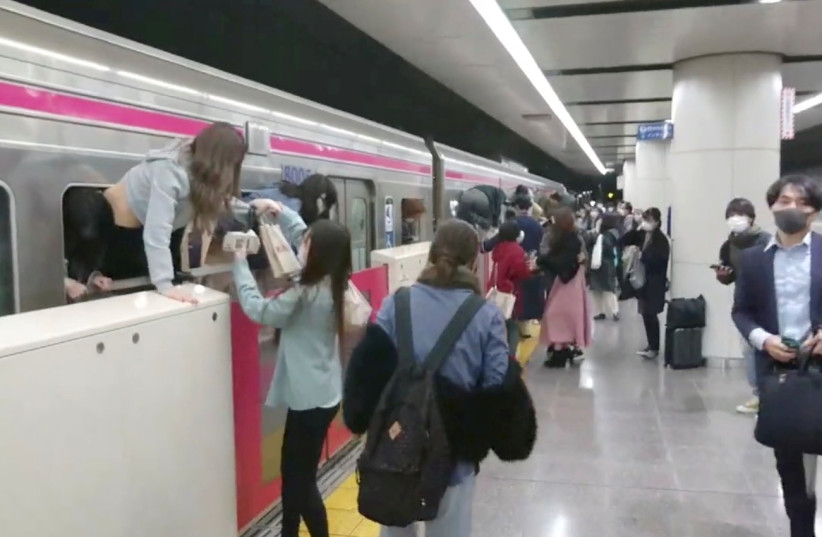 People escape through windows of a Tokyo train line following a knife and arson attack in Tokyo, Japan, October 31, 2021, in this still image obtained from a social media video. (credit: TWITTER/@SIZ33/VIA REUTERS)