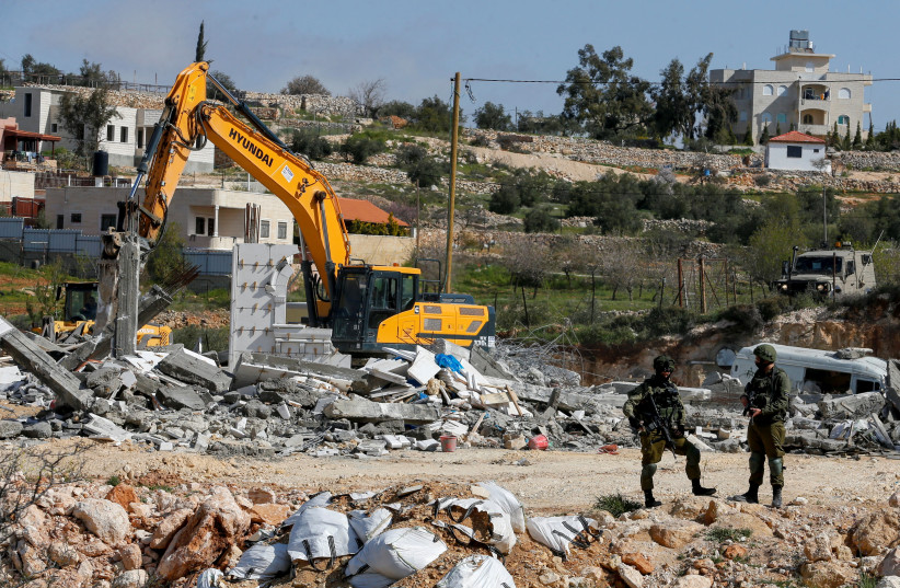 Israeli soldiers stand guard as Israeli machineries demolish an under-construction Palestinian building, in Bani Naim near Hebron in the West Bank March 8, 2021. (photo credit: MUSSA QAWASMA/REUTERS)