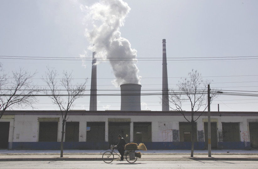 A MAN selling brooms rides his bicycle past abandoned buildings near a coal-burning power station in Beijing. (photo credit: DAVID GRAY / REUTERS)