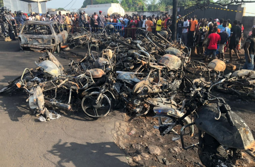 People watch burnt car and motorcycles after a fuel tanker explosion in Freetown, Sierra Leone November 6, 2021. (credit: NATIONAL DISASTER MANAGEMENT AGENCY-SIERRE LEONE/HANDOUT VIA REUTERS)