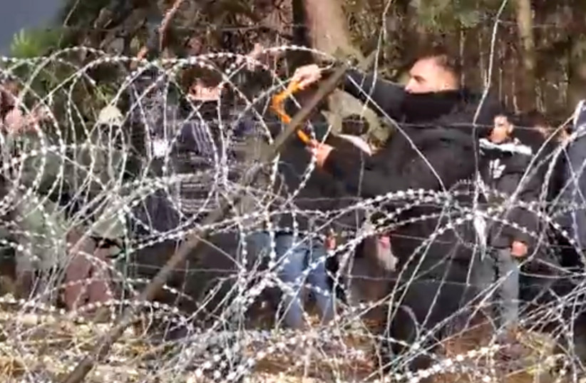 Migrants use wire cutters to cut the barbed wire as they try to cross the Belarus/Poland border near Kuznica Bialostocka, Poland, in this video-grab released by the Polish Defence Ministry, November 8, 2021. (credit: MON/HANDOUT VIA REUTERS)