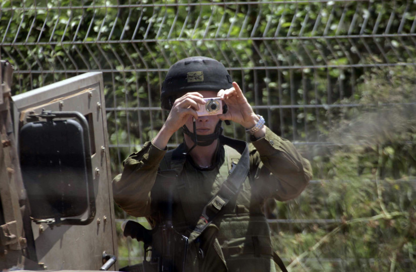  An Israeli soldier holds his camera as he patrols the Lebanese-Israeli border as seen from the southern Lebanese village of Kfar Kila, June 2, 2011 (photo credit: REUTERS/KARAMALLAH DAHER)