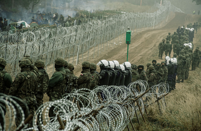  Polish soldiers and police watch migrants at the Poland/Belarus border near Kuznica, Poland, in this photograph released by the Territorial Defence Forces, November 12, 2021.  (photo credit: IREK DOROZANSKI/DWOT/HANDOUT VIA REUTERS)