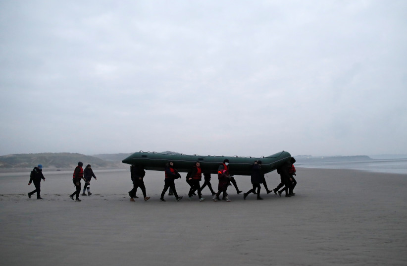  A group of more than 40 migrants run on the beach with an inflatable dinghy, as they leave the coast of northern France to cross the English Channel, near Wimereux, France, November 24, 2021 (credit: REUTERS/GONZALO FUENTES)