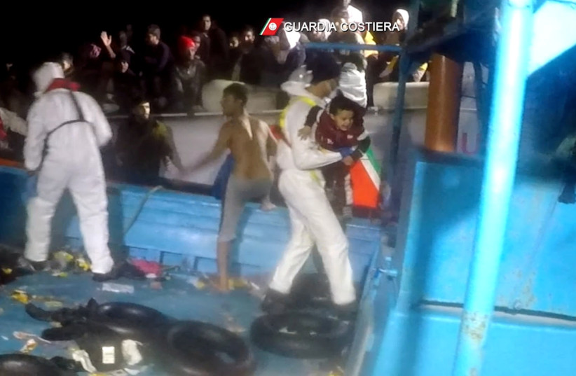  An Italian coastguard member carries a young migrant on board a coastguard vessel during a rescue operation of a boat in distress carrying migrants in the Mediterranean Sea, in this still image taken from a video, November 25, 2021 (credit: ITALIAN COAST GUARD/HANDOUT VIA REUTERS)