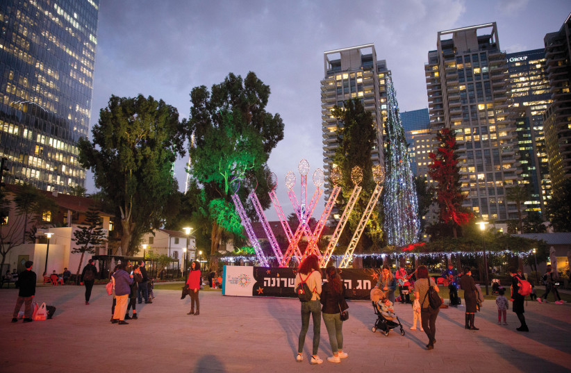  PEOPLE PASS a large hanukkiah at Tel Aviv’s Sarona Market last year. (photo credit: MIRIAM ALSTER/FLASH90)