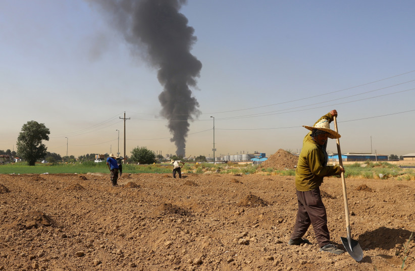  Farmers work in a field as smoke from an oil refinery rises in the background, in Tehran, Iran June 3, 2021. (photo credit: MAJID ASGARIPOUR/WANA (WEST ASIA NEWS AGENCY) VIA REUTERS)