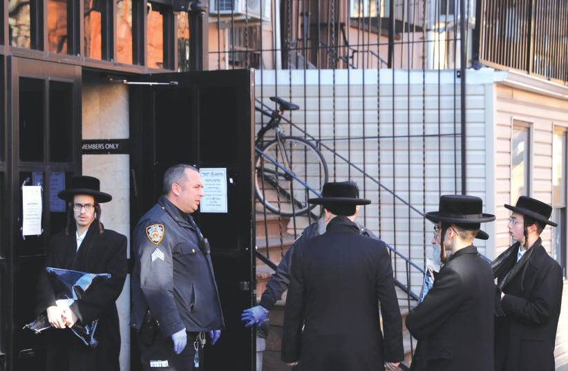 New York City police officers block hassidic men from entering a synagogue, closed due to COVID-19, in Brooklyn, in March 2020. (photo credit: ANDREW KELLY / REUTERS)