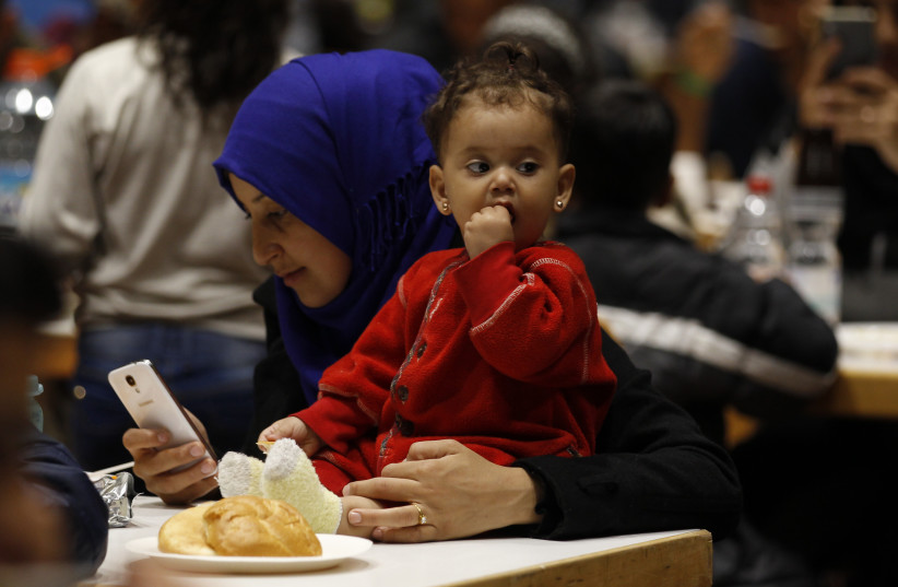 A migrant woman from Syria checks her mobile device as she eats with her daughter at a recetion centre after their arrival at the main railway station in Dortmund, Germany, September 13, 2015. (credit: REUTERS/INA FASSBENDER)