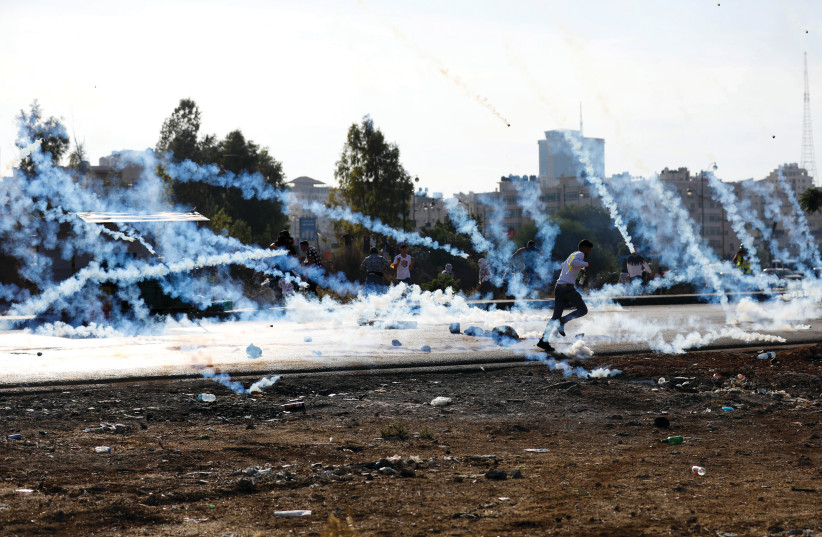  A man runs as Palestinians clash with IDF troops during a protest near Beit El. Israel should not be surprised by US opposition to settlement construction. (photo credit: MOHAMAD TOROKMAN/REUTERS)
