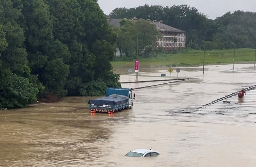 Partially submerged cars are seen on a flooded road in Shah Alam, Malaysia December 18, 2021, in still image obtained from social media video. (photo credit: COURTESY/ASHRAF NOOR AZAM/VIA REUTERS)