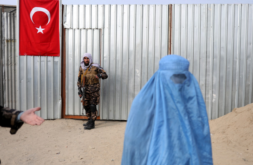  A Taliban fighter is seen as a woman arrives to receive a package being distributed by a Turkish humanitarian aid group at a distribution centre in Kabul, Afghanistan, December 15, 2021.  (photo credit:  REUTERS/ALI KHARA)