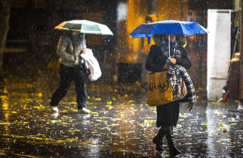  People take cover from the rain as they walk on Jaffa Road  in the city center of Jerusalem on December 20, 2021. (credit: OLIVIER FITOUSSI/FLASH90)