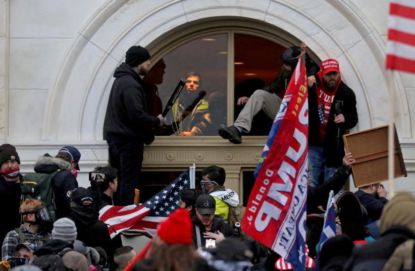A mob of supporters of then-US President Donald Trump climb through a window they broke as they storm the US Capitol Building in Washington, US, January 6, 2021. (photo credit: REUTERS/LEAH MILLIS/FILE PHOTO)