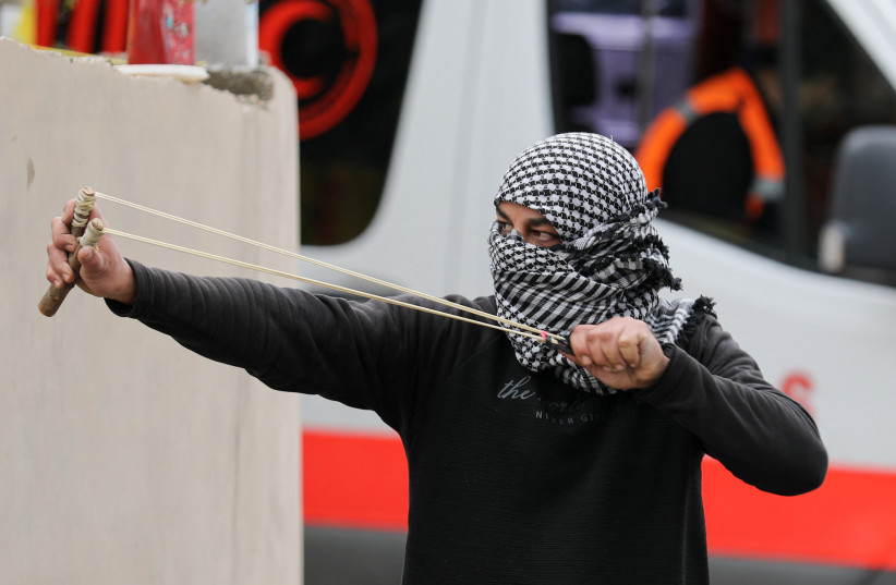  A Palestinian demonstrator uses a slingshot during a protest against Jewish settlements, in Burqa village, in the West Bank December 23, 2021. (credit: REUTERS/RANEEN SAWAFTA)
