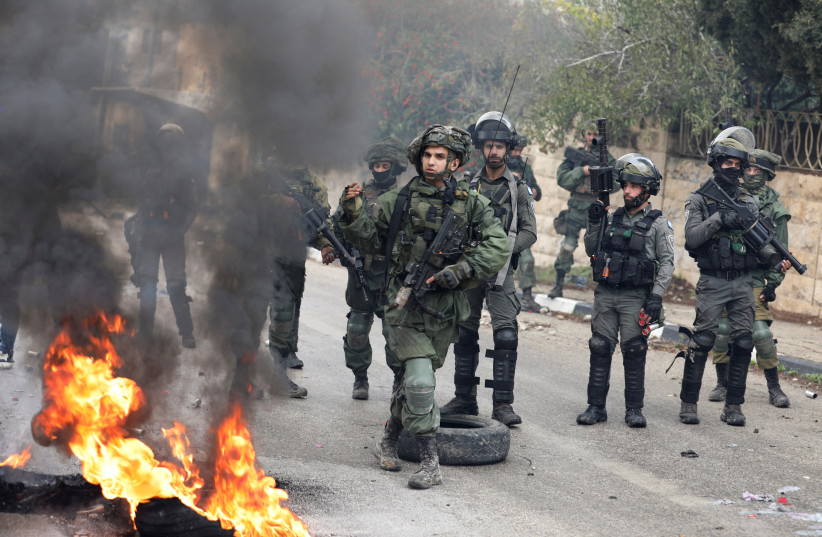  Des membres des forces israéliennes se tiennent à côté d'une barricade en feu lors d'une manifestation contre les colonies juives, dans le village de Burqa, en Cisjordanie, le 23 décembre 2021. (Crédit : REUTERS/RANEEN SAWAFTA)