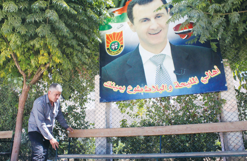  A SYRIAN MAN adjusts a chair near a poster depicting Syria’s President Bashar Assad, in Mleiha, earlier this year.  (photo credit: FIRAS MAKDESI/REUTERS)