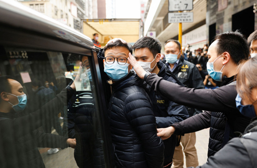 Stand News acting chief editor Patrick Lam, one of the six people arrested "for conspiracy to publish seditious publication" according to Hong Kong's Police National Security Department, is escorted by police as they leave after the police searched his office in Hong Kong, China, December 29, 2021. (photo credit: REUTERS/TYRONE SIU)