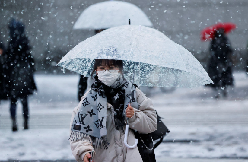  A woman wearing a protective face mask walks on a street in snowfall, amid the coronavirus disease (COVID-19) pandemic, in Tokyo, Japan January 6, 2022.  (credit: REUTERS/ISSEI KATO)