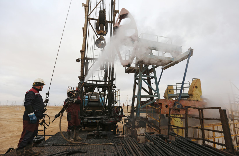  Workers use a steam jet to clean an oil pump in the Uzen oil and gas field in the Mangistau Region of Kazakhstan November 13, 2021. (photo credit: REUTERS/PAVEL MIKHEYEV)