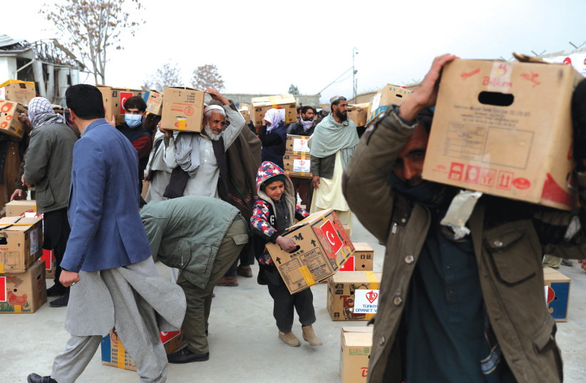 Afghans carrying packages handed out by a Turkish humanitarian aid group at a distribution center in Kabul last month. President Joe Biden betrayed the Afghans. (photo credit: ALI KHARA/REUTERS)