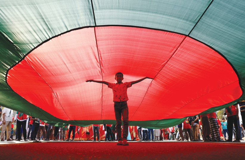  A boy poses under a massive Bangladeshi flag in front of the parliamentary building in Dhaka, celebrating the country’s 50th Victory Day anniversary. (photo credit: REUTERS/MOHAMMAD PONIR HOSSAIN)