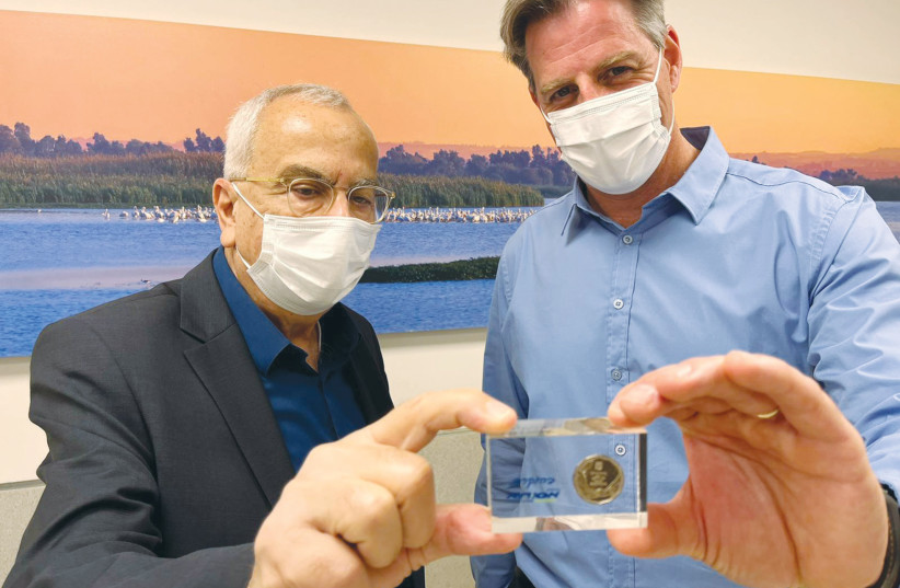 Prof. Shuki Shemer (left) and Gidi Leshetz, chairman and CEO respectively of Assuta Medical Center, hold up the NUS5 coin special minted in honor of Israel’s medical teams. (credit: ASSUTA)