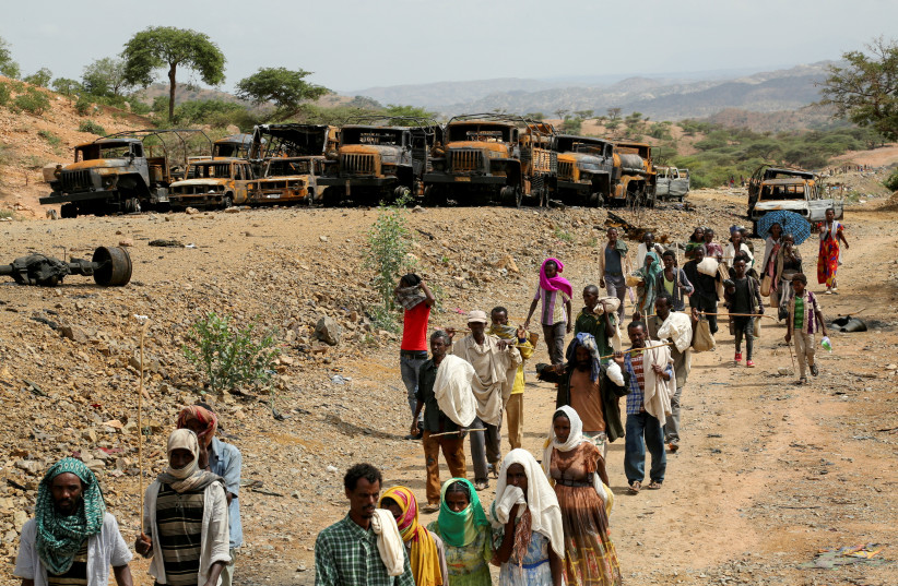 Villagers return from a market to Yechila town in south central Tigray walking past scores of burned vehicles, in Tigray, Ethiopia, July 10, 2021. (photo credit: REUTERS/GIULIA PARAVICINI/FILE PHOTO)