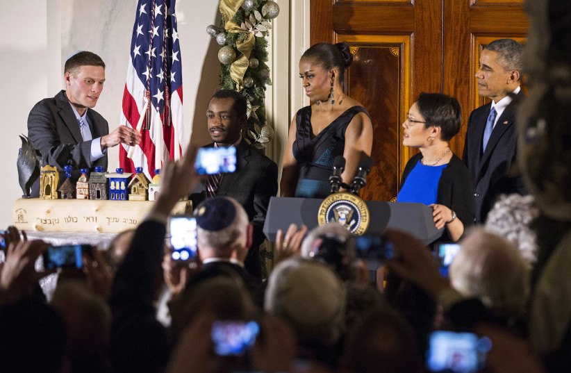 US President Barack Obama (R), first lady Michelle Obama (C) and Rabbi Angela Buchdahl (2nd R) watch as Dr. Adam Levine (L) and Ataklit Tesfaye (2nd L) light a menorah at a Hanukkah reception in the Grand Foyer of the White House in Washington, December 17, 2014. (credit: REUTERS/JOSHUA ROBERTS)