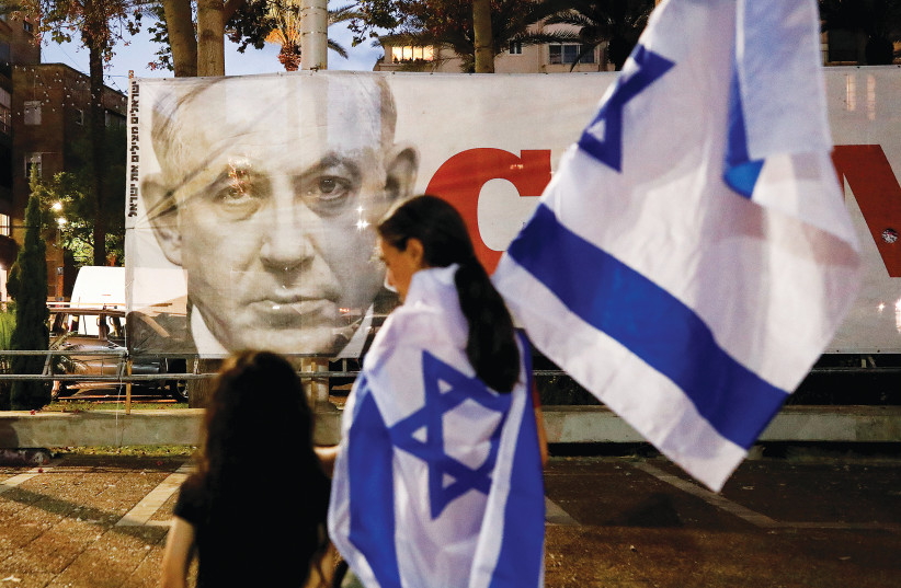  PEDESTRIANS WALK past a banner protesting former prime minister Benjamin Netanyahu, in Tel Aviv last year. (photo credit: CORINNA KERN/REUTERS)