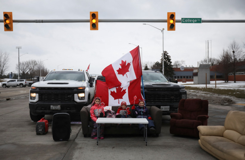  Children sit on a sofa placed on a blocked road as the Ambassador Bridge, which connects Detroit and Windsor, stands effectively shut down after truckers and their supporters blocked it in protest against coronavirus disease (COVID-19) vaccine mandates, in Windsor, Ontario, Canada February 10, 2022 (photo credit: REUTERS/CARLOS OSORIO)